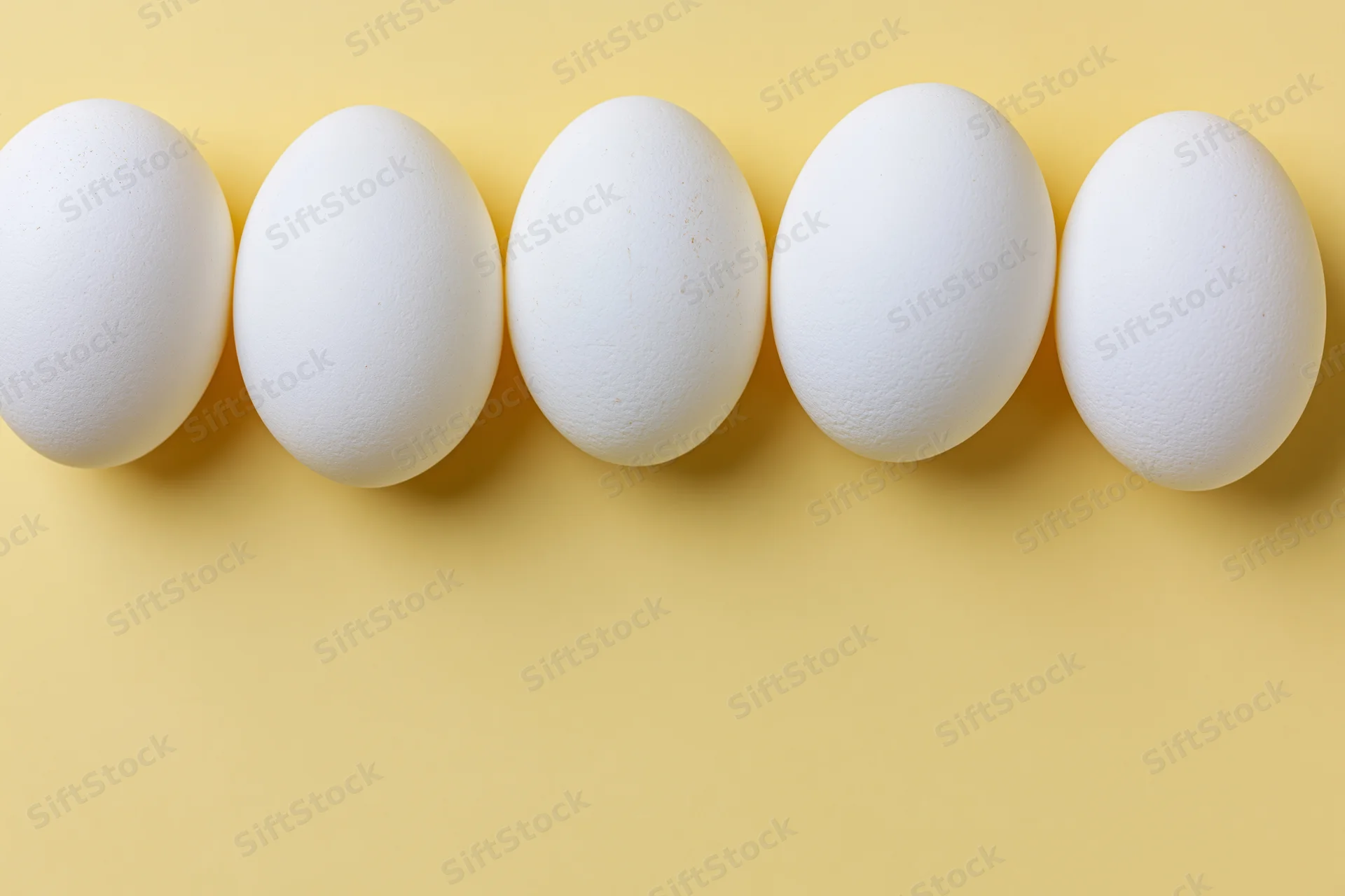 Five white chicken eggs arranged in a horizontal row on a yellow background