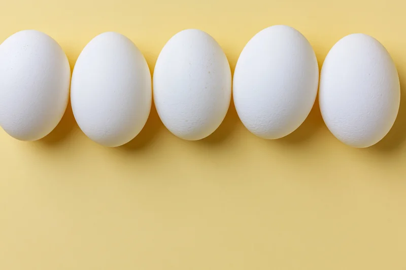 Five white chicken eggs arranged in a horizontal row on a yellow background