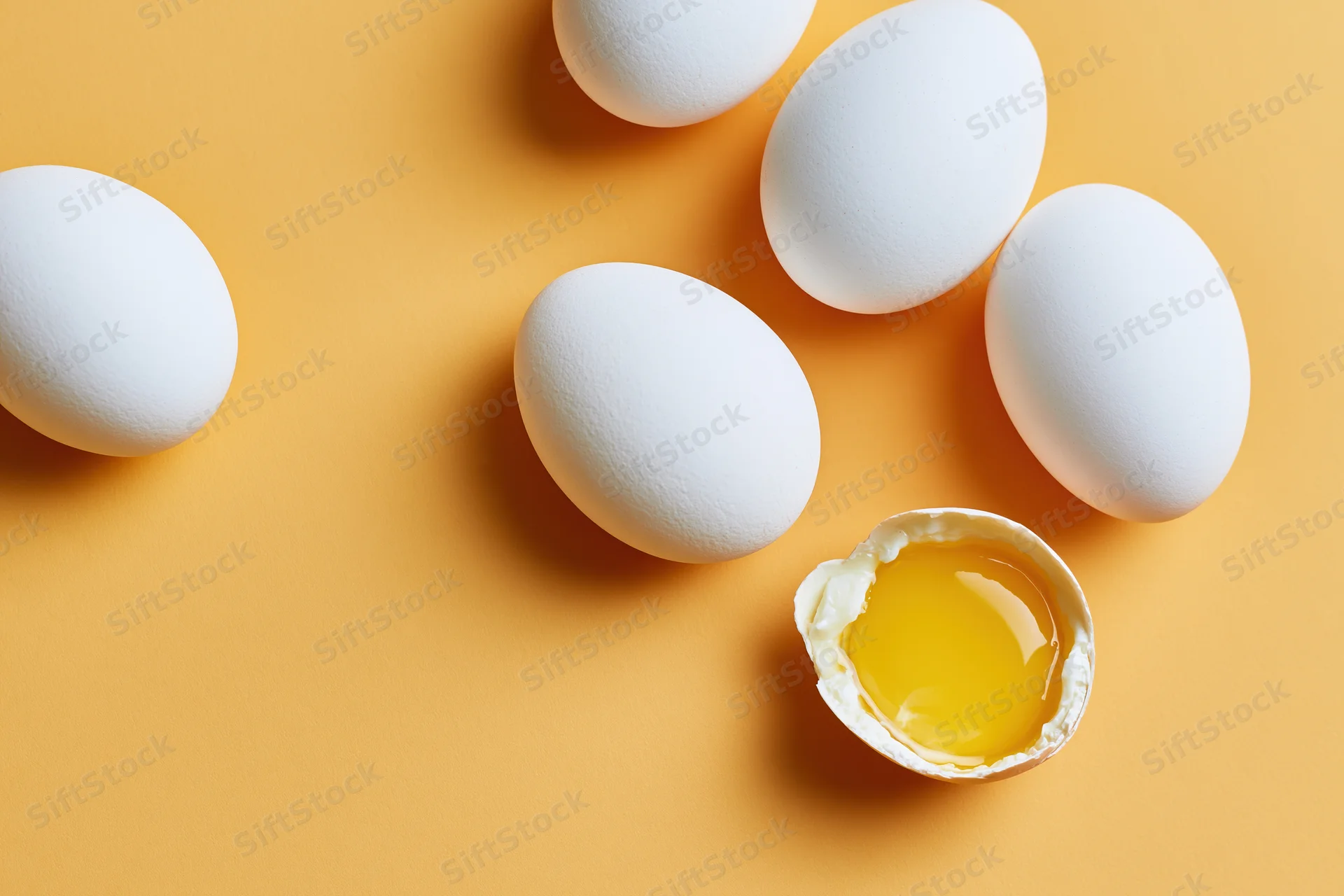 White eggs scattered on orange surface with one cracked open showing yolk