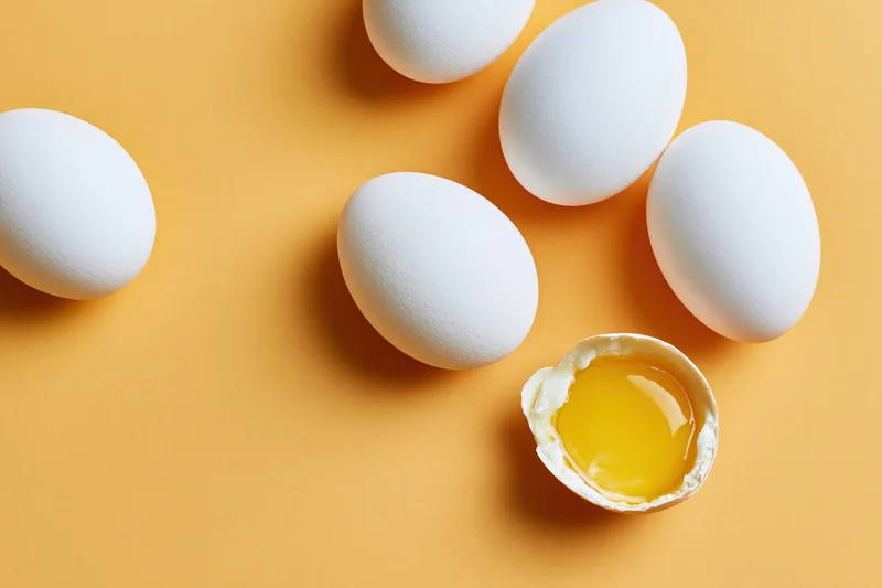White eggs scattered on orange surface with one cracked open showing yolk