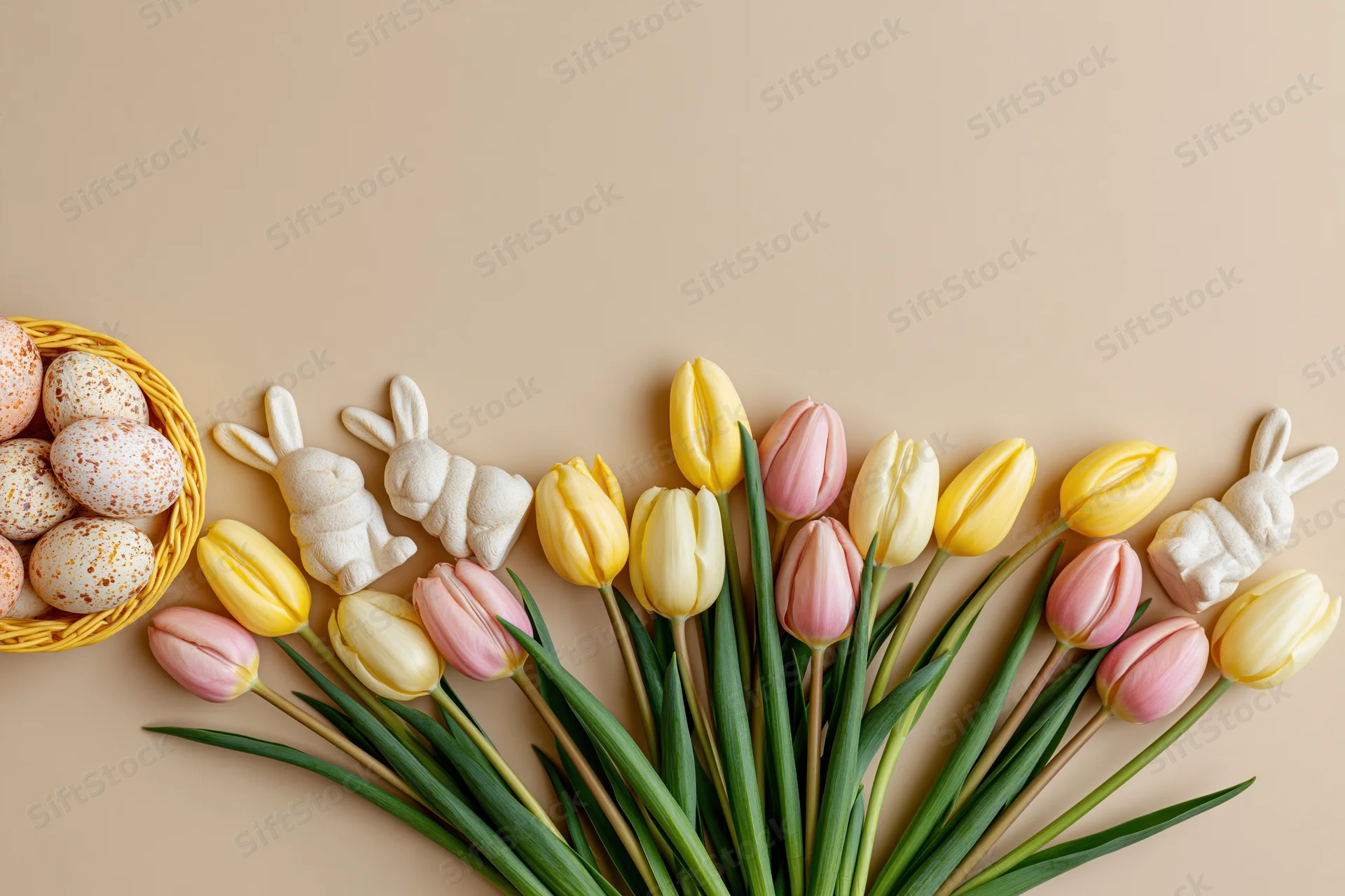 Easter flat lay with tulips, speckled eggs in a basket, and sugar bunnies arranged along the bottom edge of a beige surface