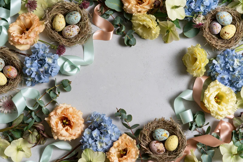 Easter floral arrangement forming a decorative border around a gray surface with nests, eggs, and ribbons