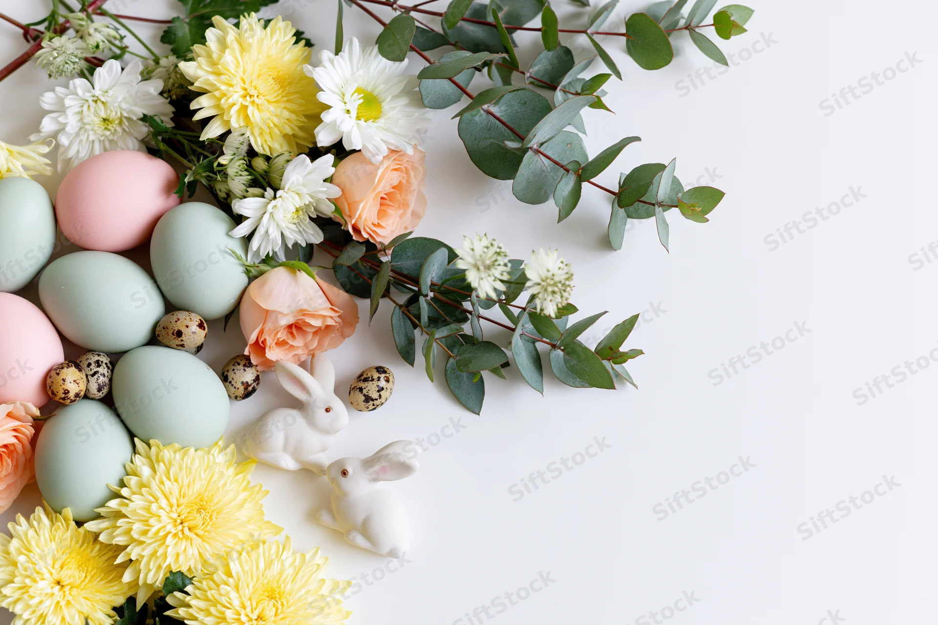 Easter arrangement with pastel eggs, flowers, and ceramic bunnies in flat lay style on white background