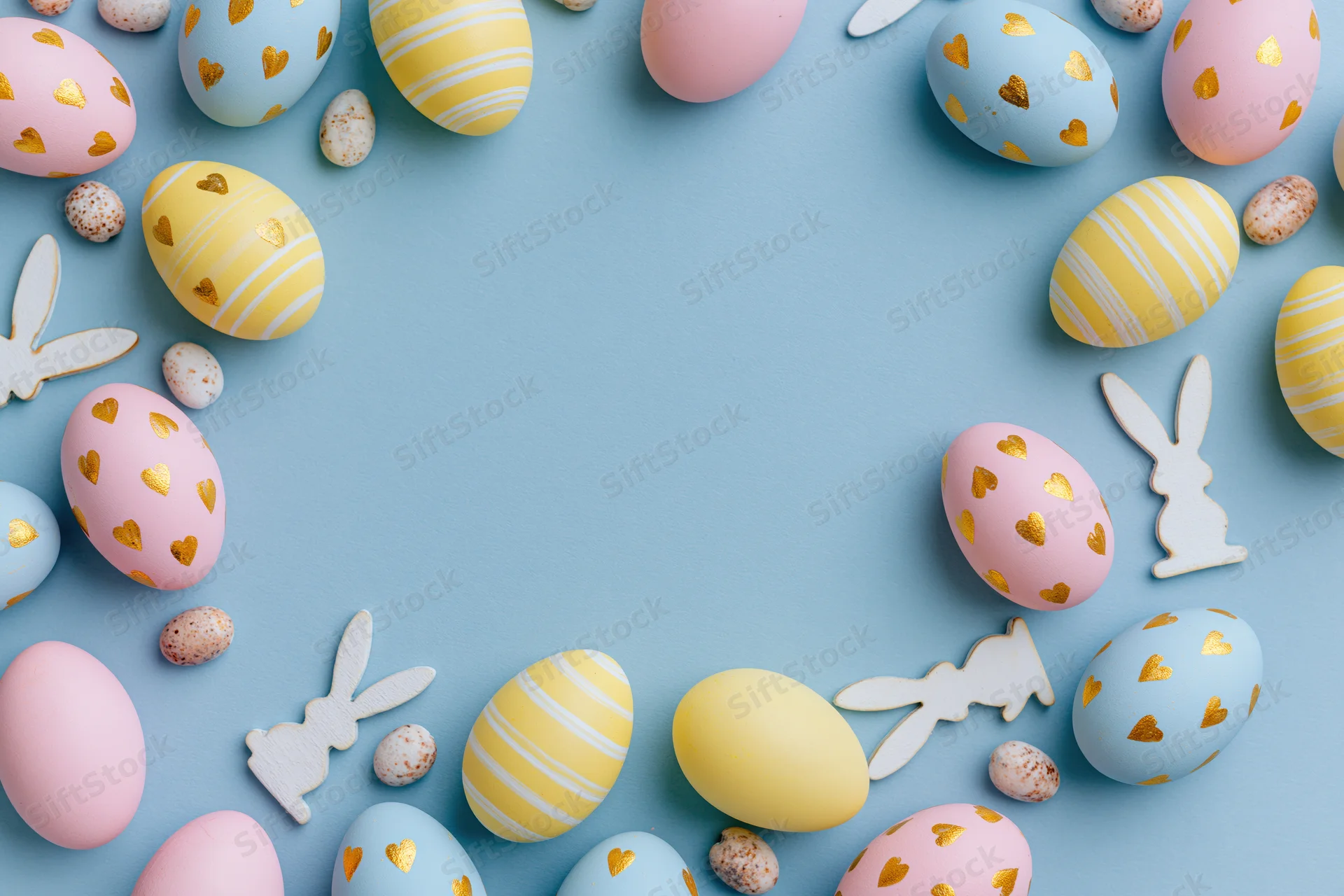 Flat lay arrangement of pastel easter eggs and wooden bunny cutouts on blue background
