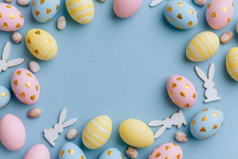 Flat lay arrangement of pastel easter eggs and wooden bunny cutouts on blue background