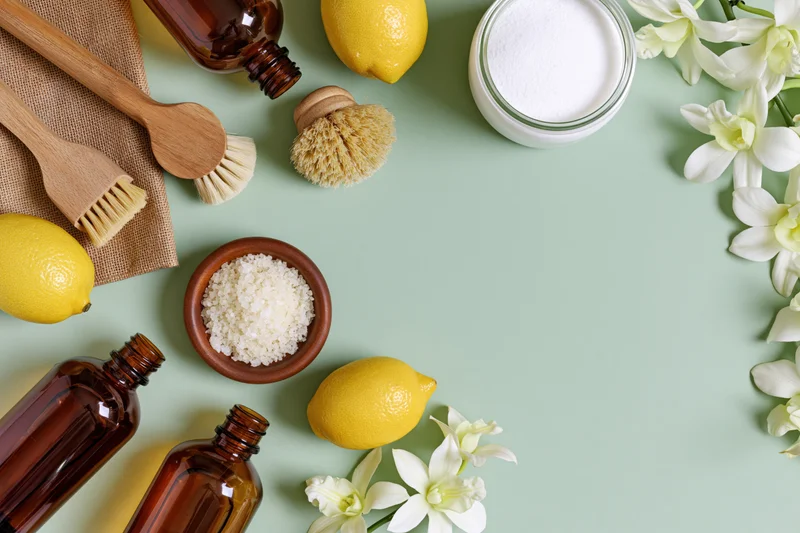 Flat lay of eco-friendly cleaning supplies arranged on a mint green surface with lemons, flowers, and wooden tools