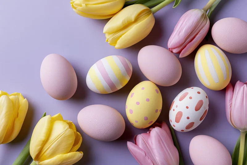 Easter eggs and tulips arranged in a flat lay on a pastel purple surface