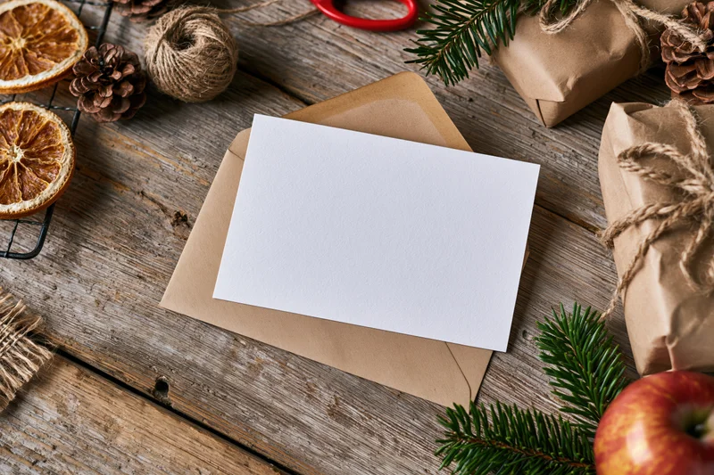 Blank white card on kraft envelope with christmas decorations on wooden surface