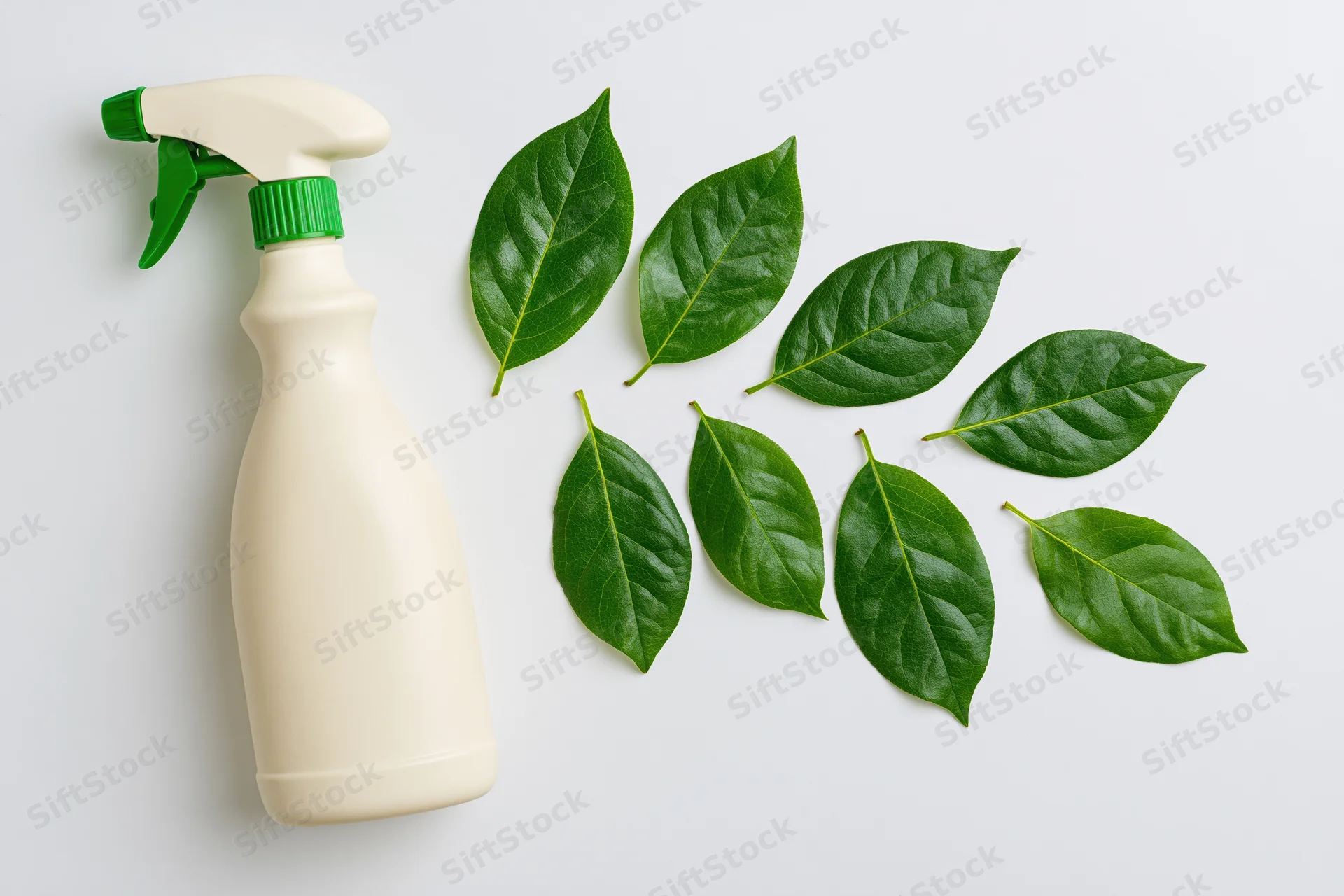 Cream-colored plastic spray bottle with green nozzle and cap arranged flat on white surface beside scattered green leaves