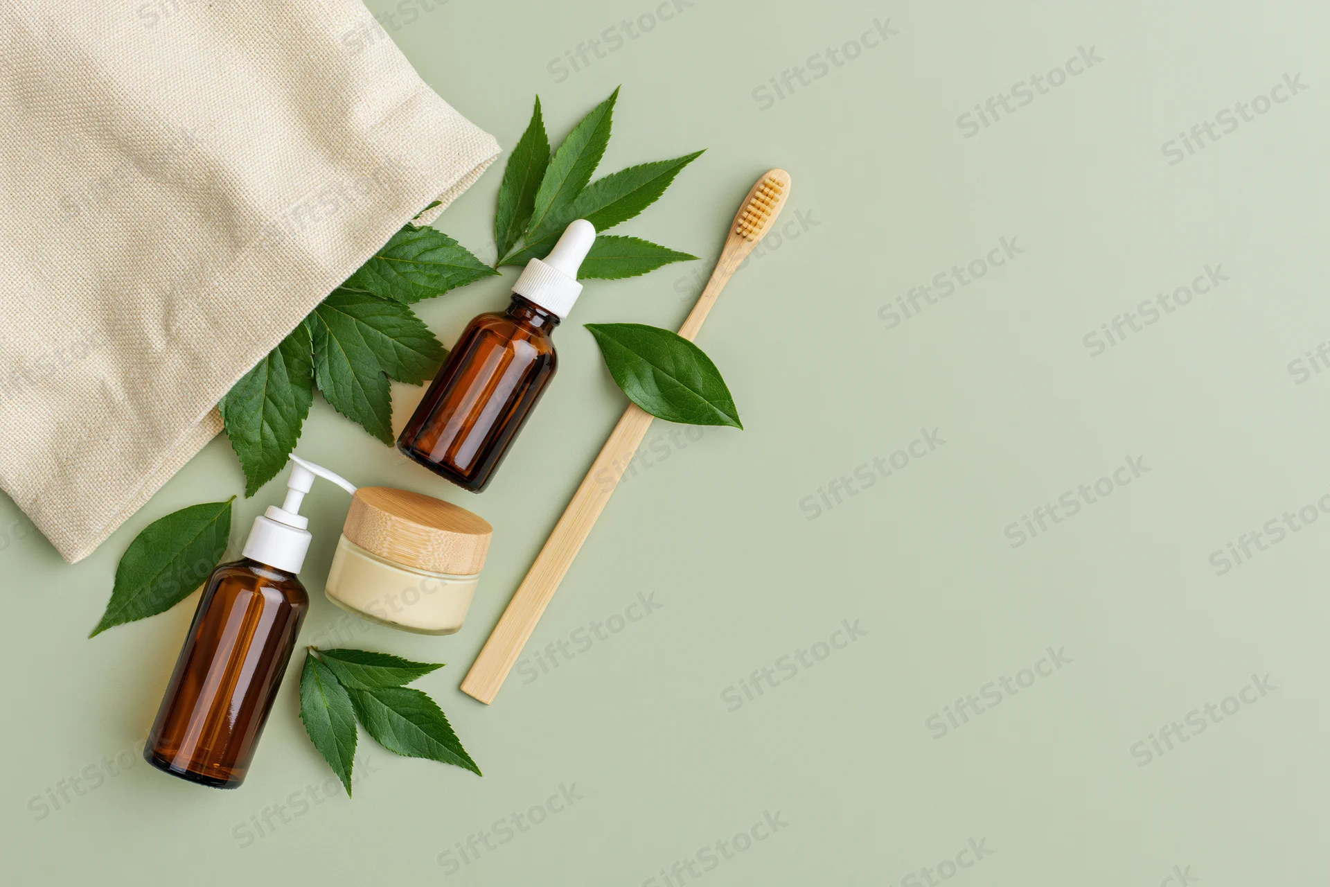 Natural skincare products and bamboo toothbrush arranged with green leaves on a flat surface beside a canvas tote bag