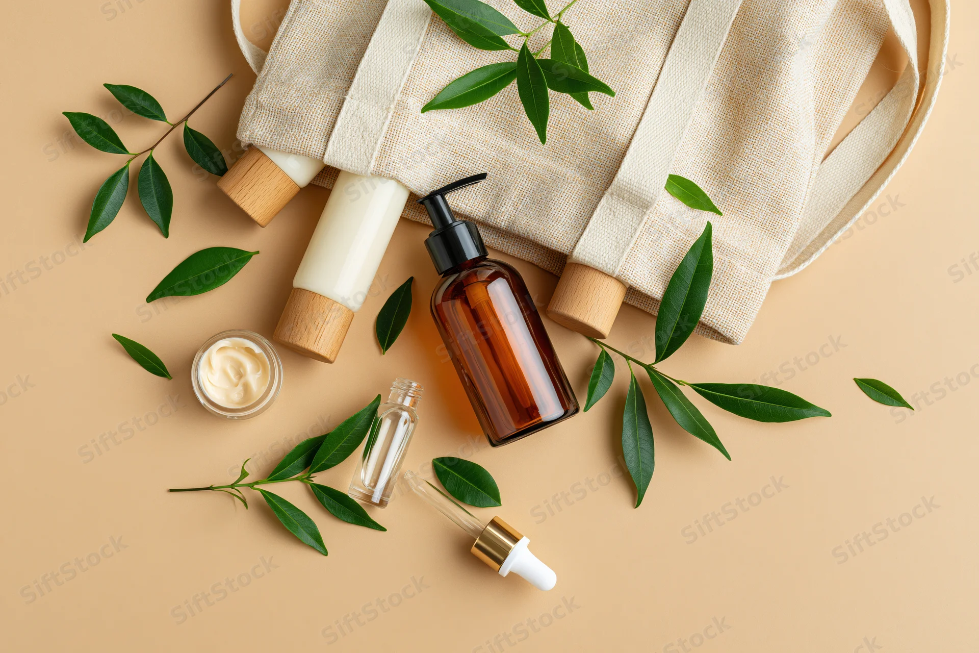 Flat lay of skincare products with green leaves and a canvas tote bag on beige background