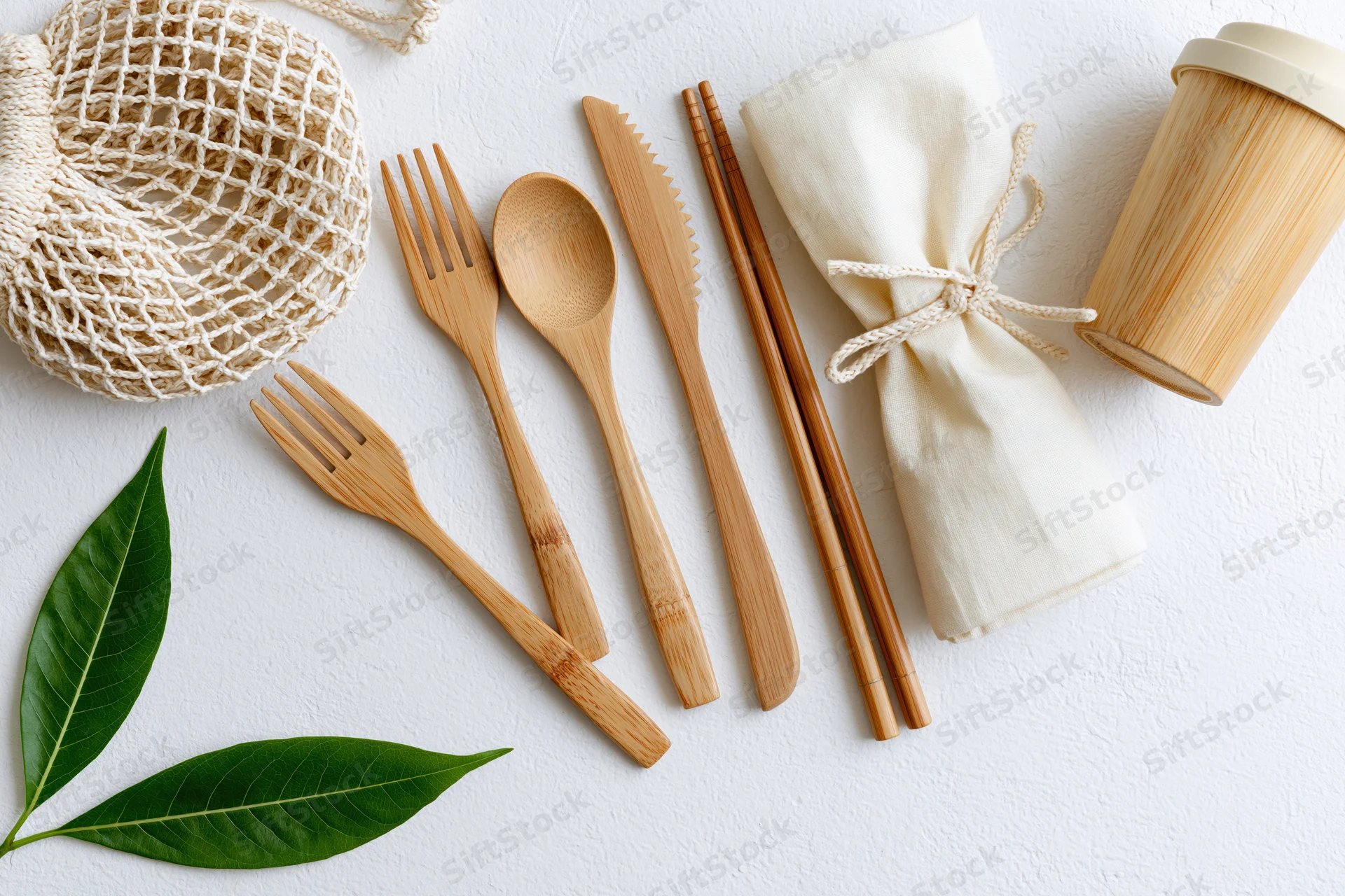Bamboo cutlery set arranged flat on white surface with leaves and reusable bag