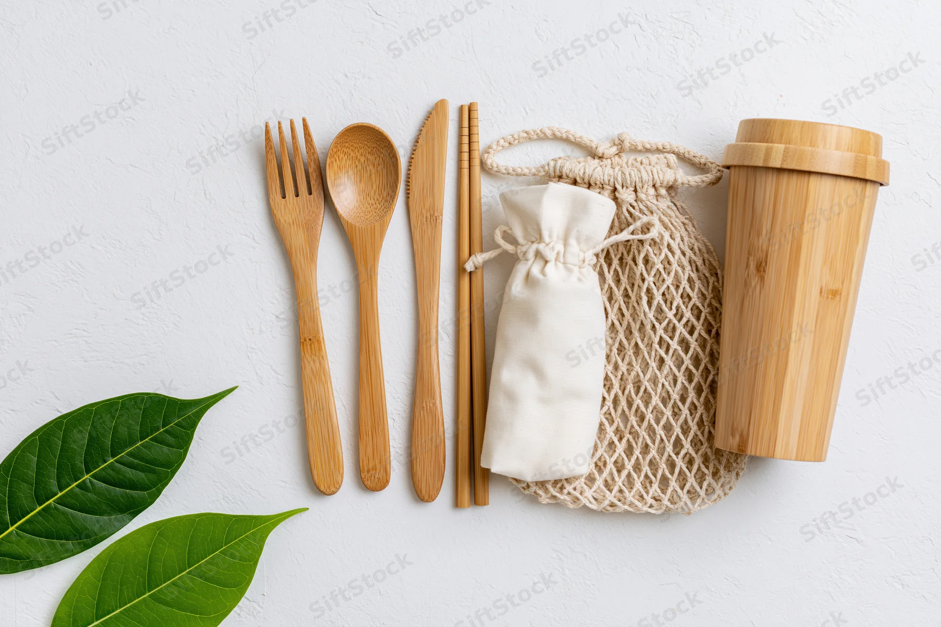Bamboo cutlery set arranged flat on white surface with green leaves and storage bags
