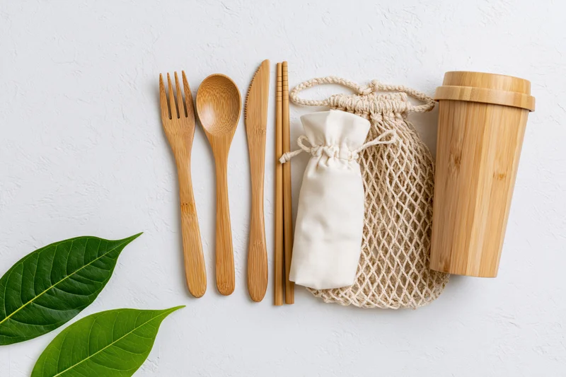 Bamboo cutlery set arranged flat on white surface with green leaves and storage bags