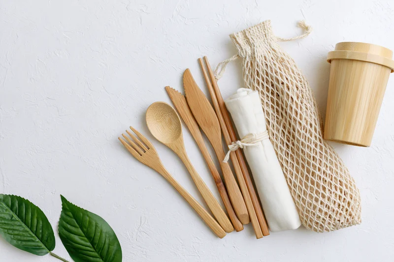 Bamboo cutlery set including fork spoon knife chopsticks arranged with mesh bag and cup on white surface