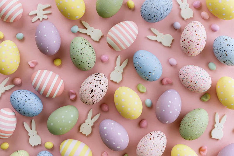 Colorful pastel easter eggs with striped and polka dot patterns arranged in flat lay on pink surface with bunny decorations