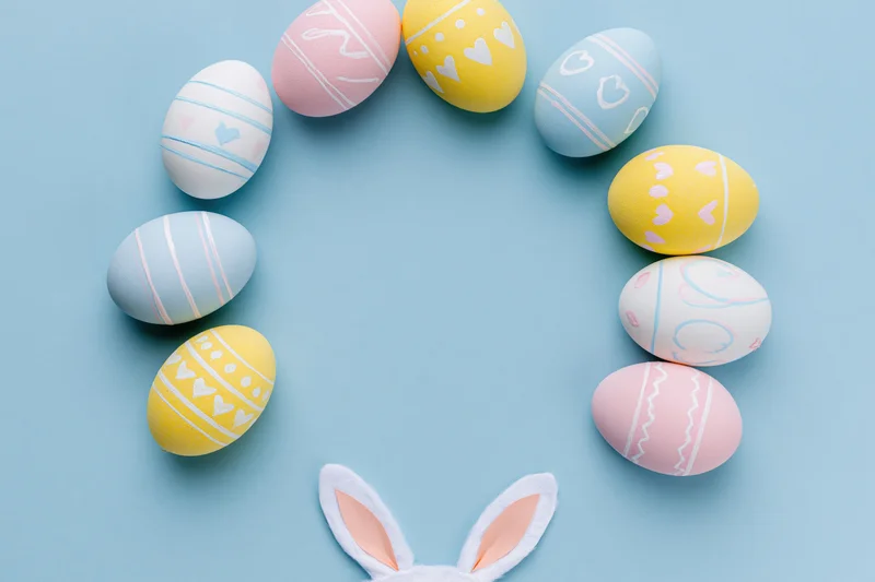 Decorated easter eggs arranged in a circle with bunny ears on a pastel blue background