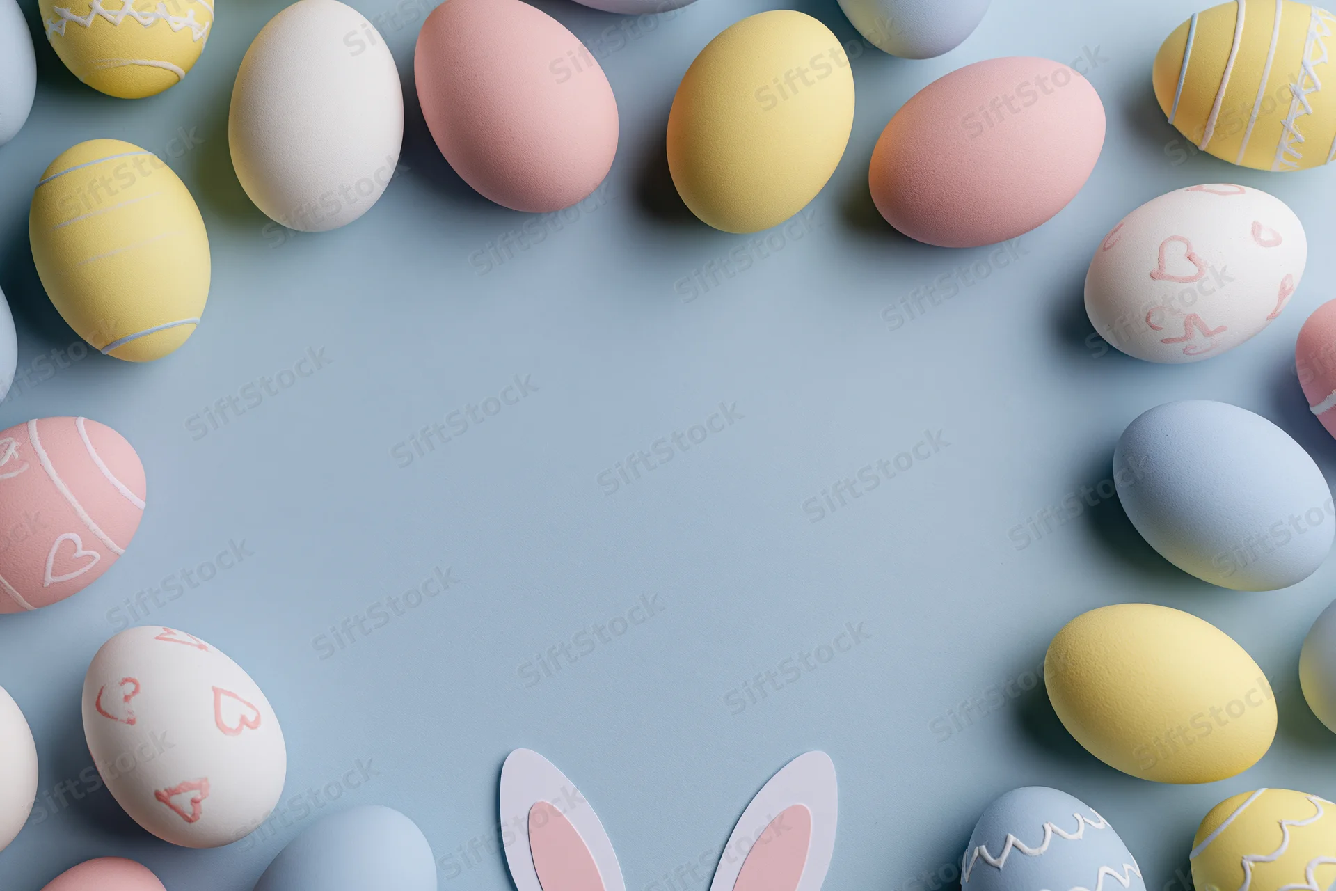 Decorated easter eggs arranged in a frame on a pastel blue surface with bunny ears and copyspace in center