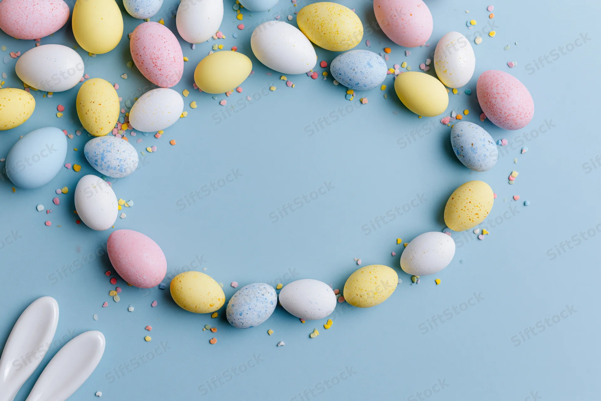 Decorated easter eggs arranged in a circular frame on a pastel blue surface with copyspace in the center