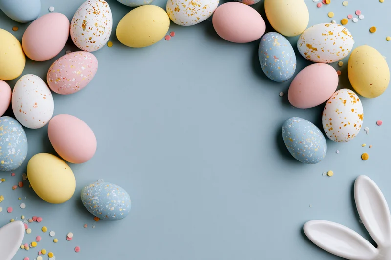 Decorated easter eggs arranged in a frame on a pastel blue surface with bunny ears and confetti