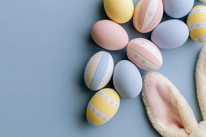Decorated easter eggs in pastel colors arranged with plush bunny ears on a flat surface