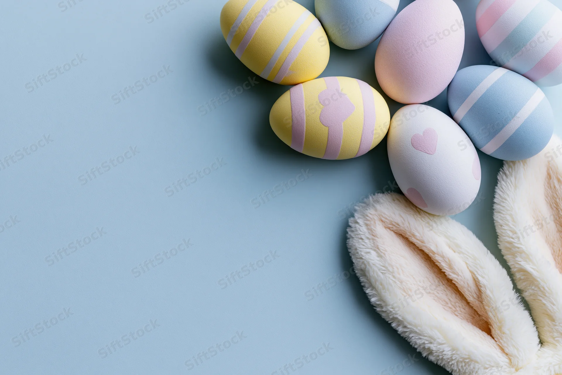 Decorated easter eggs and bunny ears arranged in flat lay on pastel blue surface with copyspace