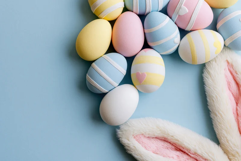 Decorated easter eggs and bunny ears arranged in a flat lay on a blue surface