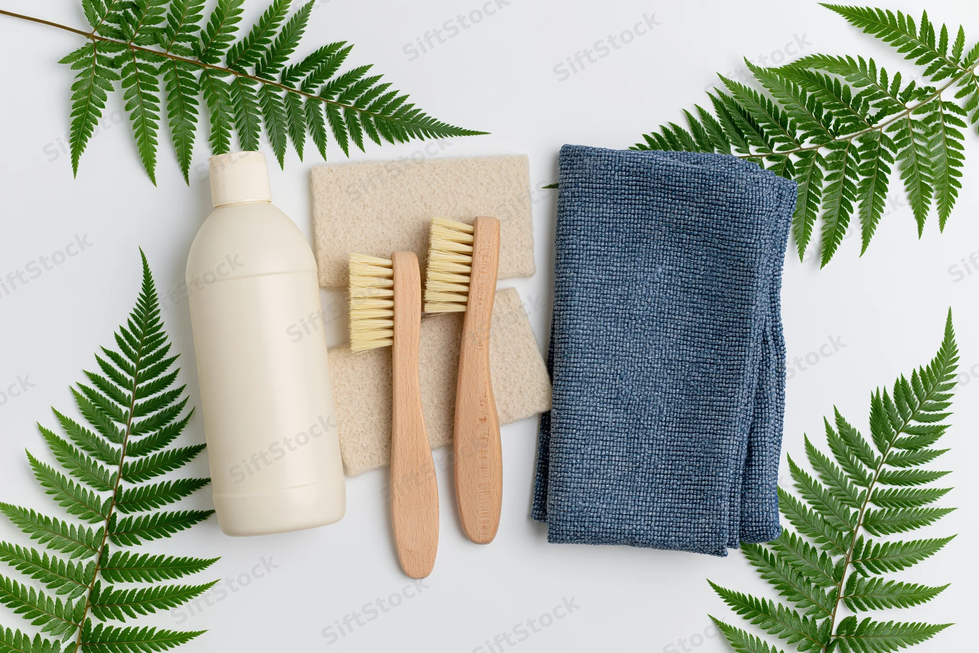 Eco-friendly cleaning supplies arranged in flat lay on white surface with fern leaves