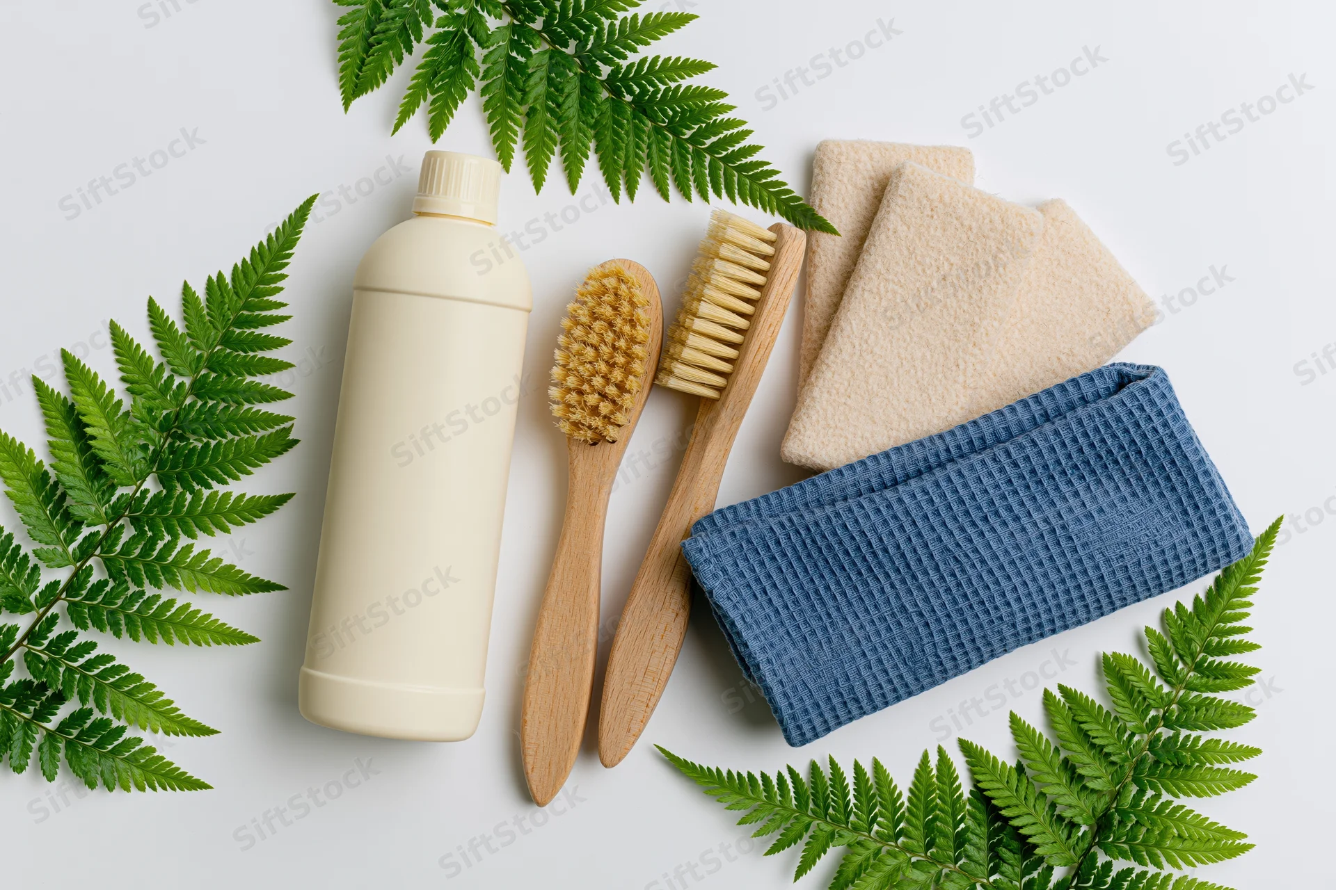 Eco-friendly cleaning supplies arranged in flat lay on white surface with fern leaves