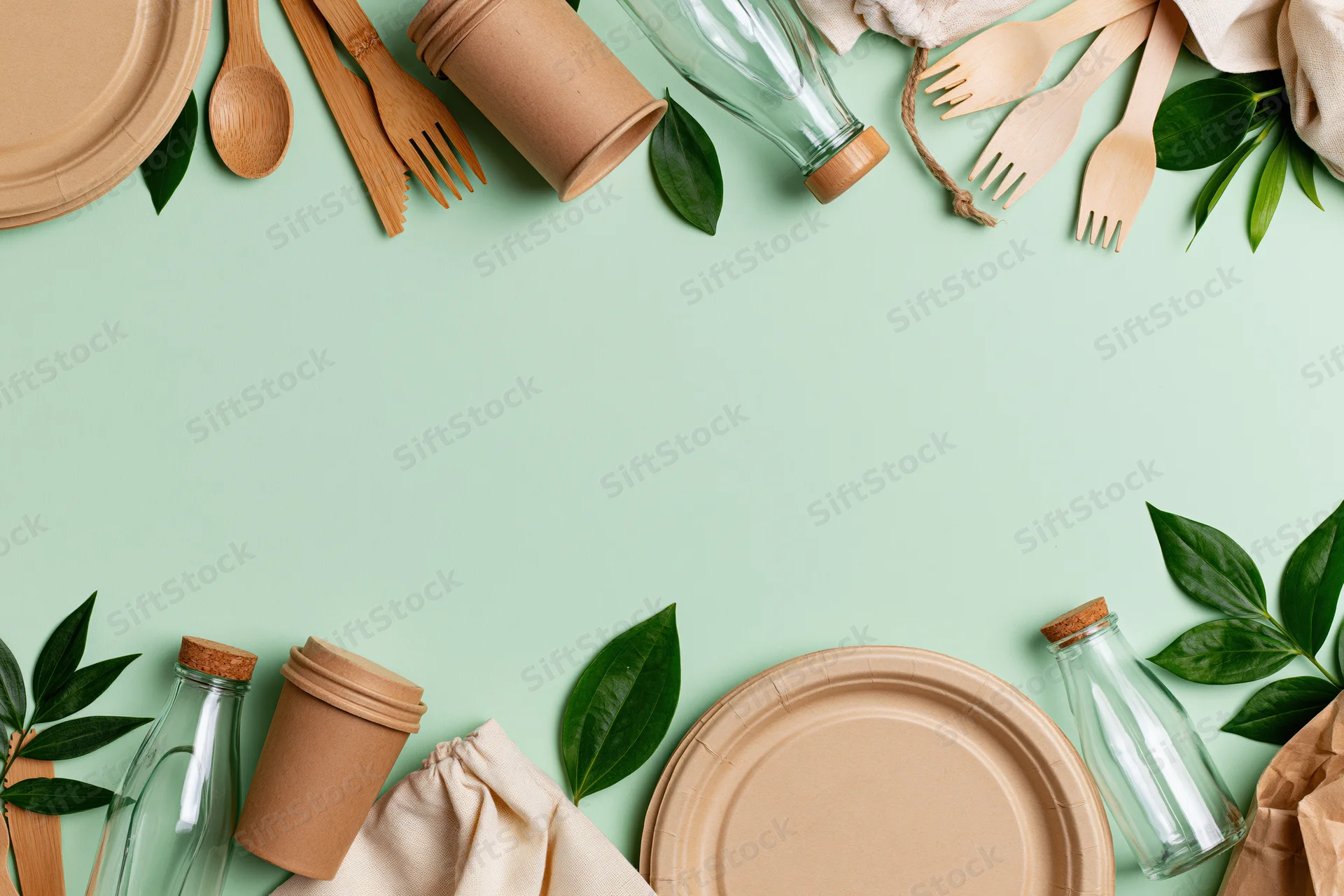 Eco-friendly disposable tableware arranged in a flat lay with green leaves on a mint background