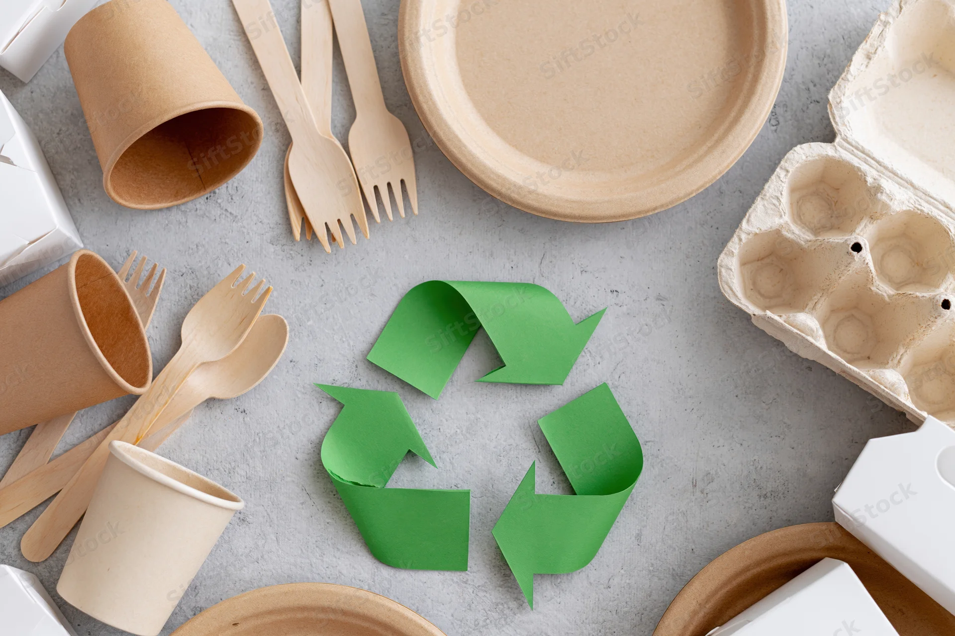 Eco-friendly disposable tableware arranged in flat lay on gray surface with recycling symbol in center