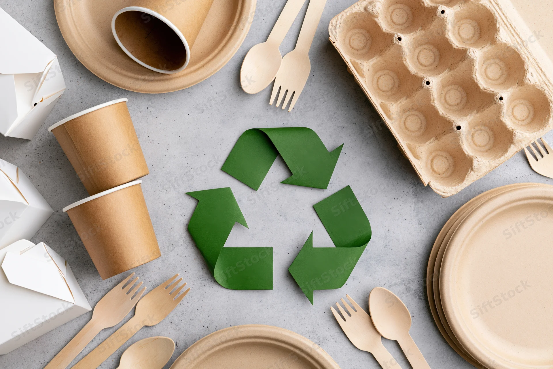 Eco-friendly disposable tableware arranged in flat lay around recycling symbol on gray surface