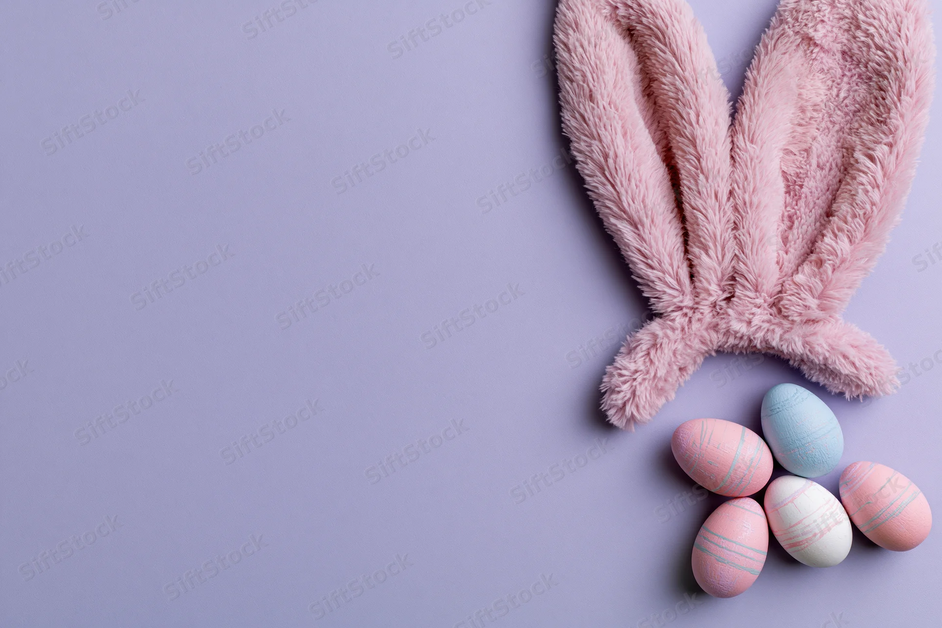Fluffy pink plush bunny ears and decorated pastel eggs arranged on a lavender surface in a flat lay composition