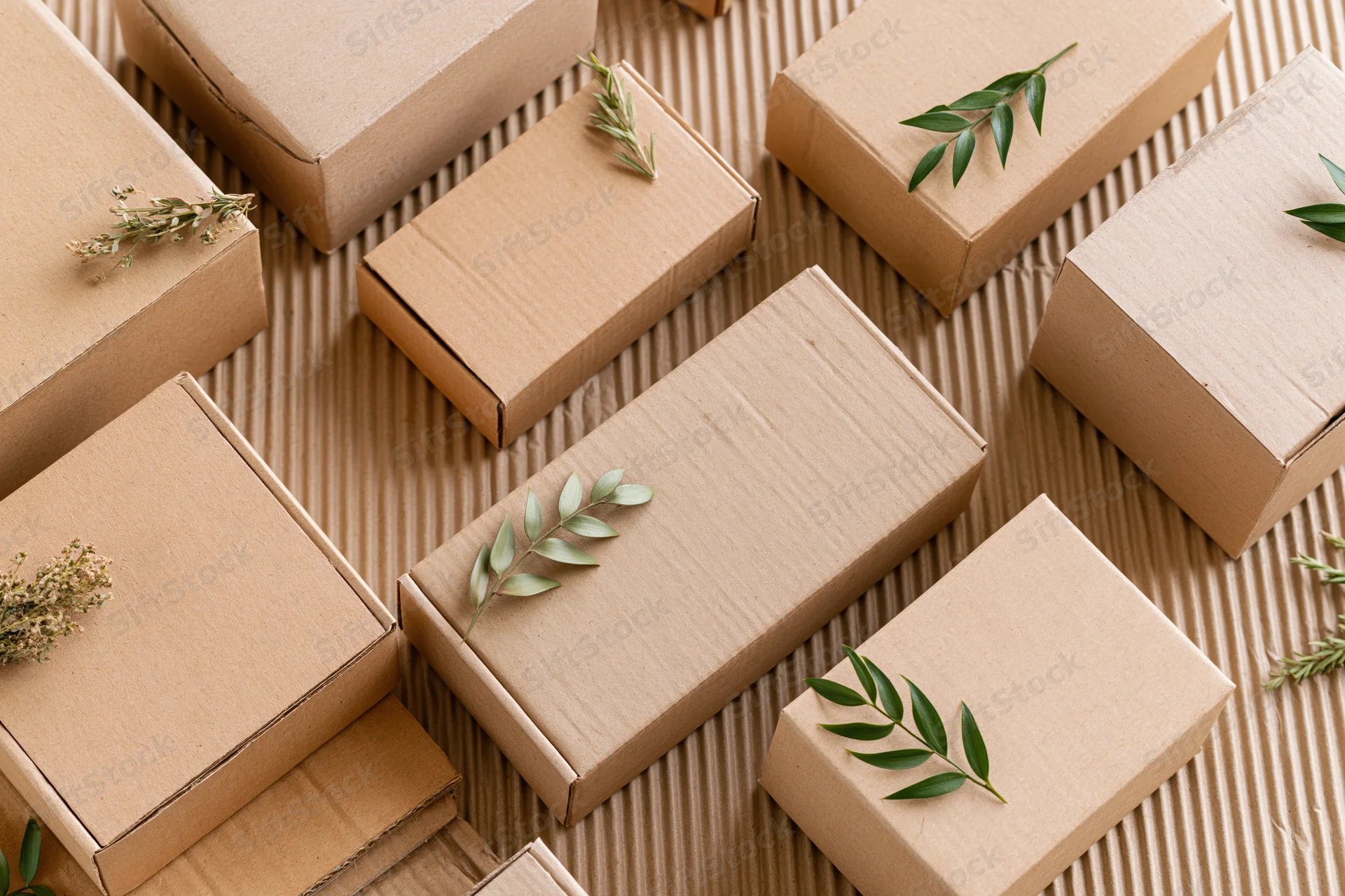Multiple kraft cardboard boxes arranged in flat lay with greenery on textured surface