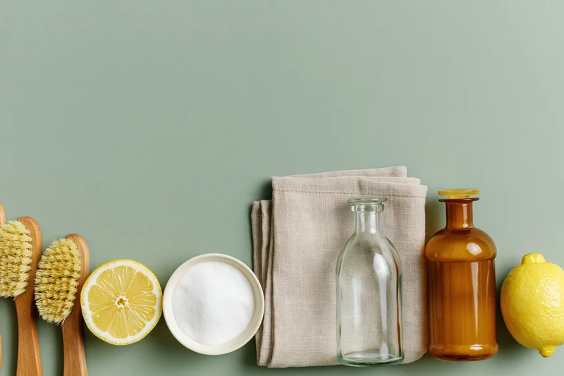 Natural cleaning supplies arranged in a flat lay on a green background