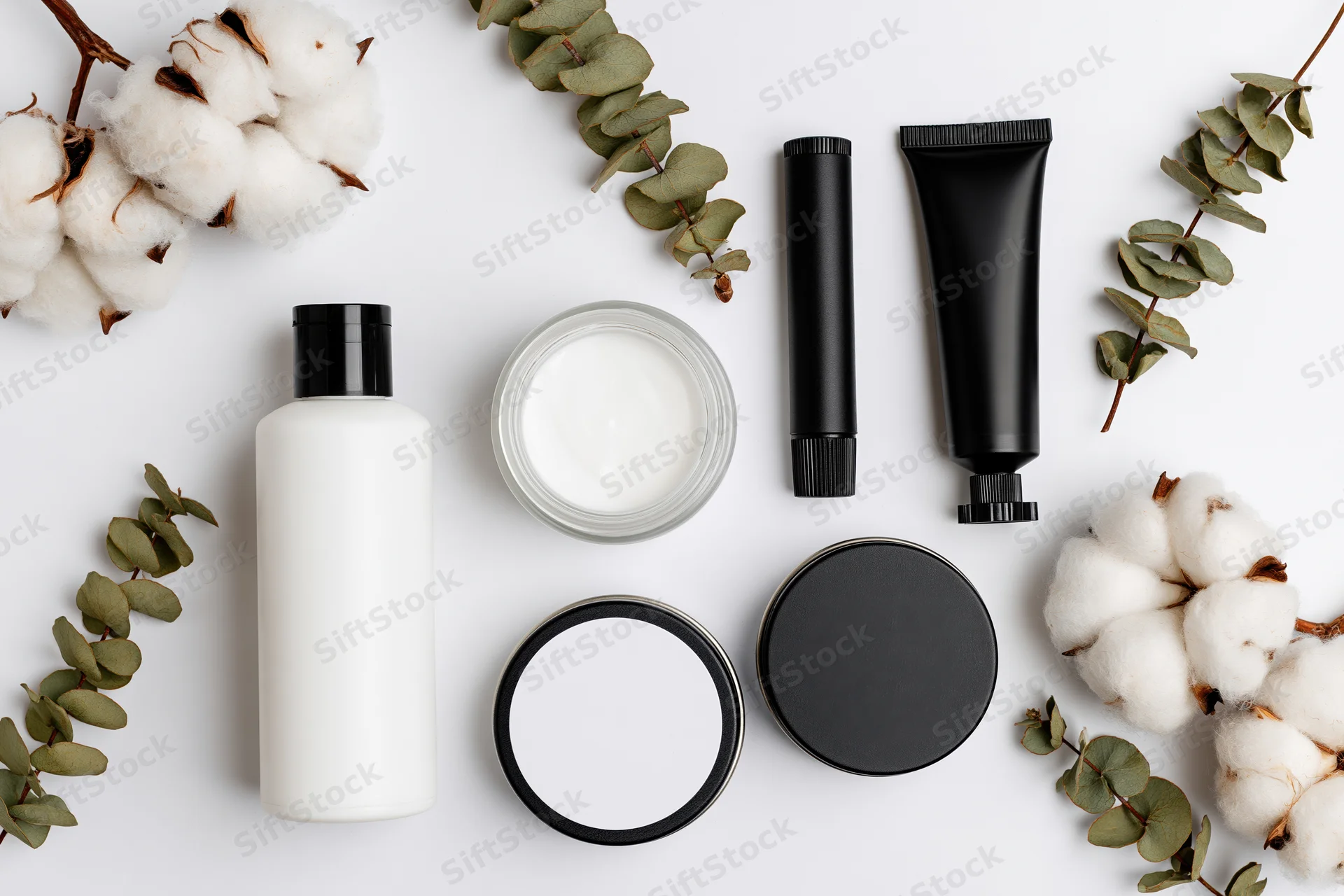 Flat lay of skincare products with cotton and eucalyptus on white background