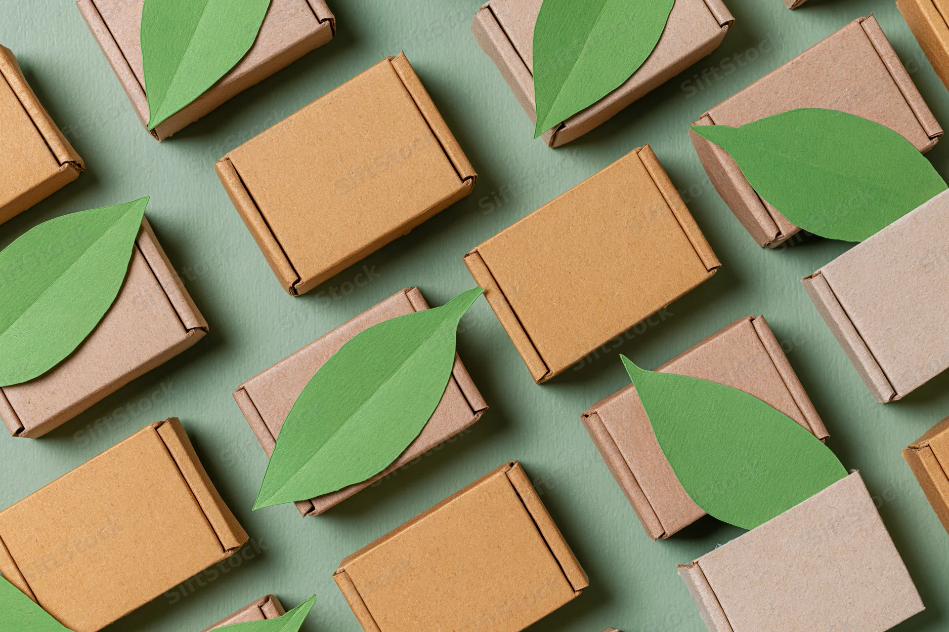Small corrugated cardboard shipping boxes arranged in flat lay with green leaves on muted green background
