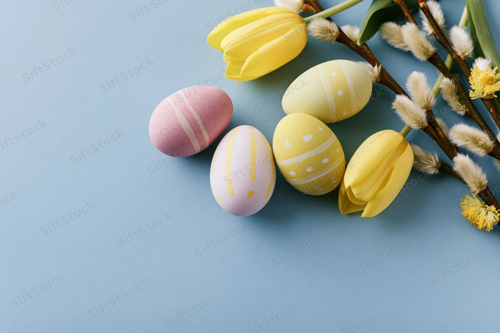 Hand-painted easter eggs and spring flowers arranged in flat lay on blue background