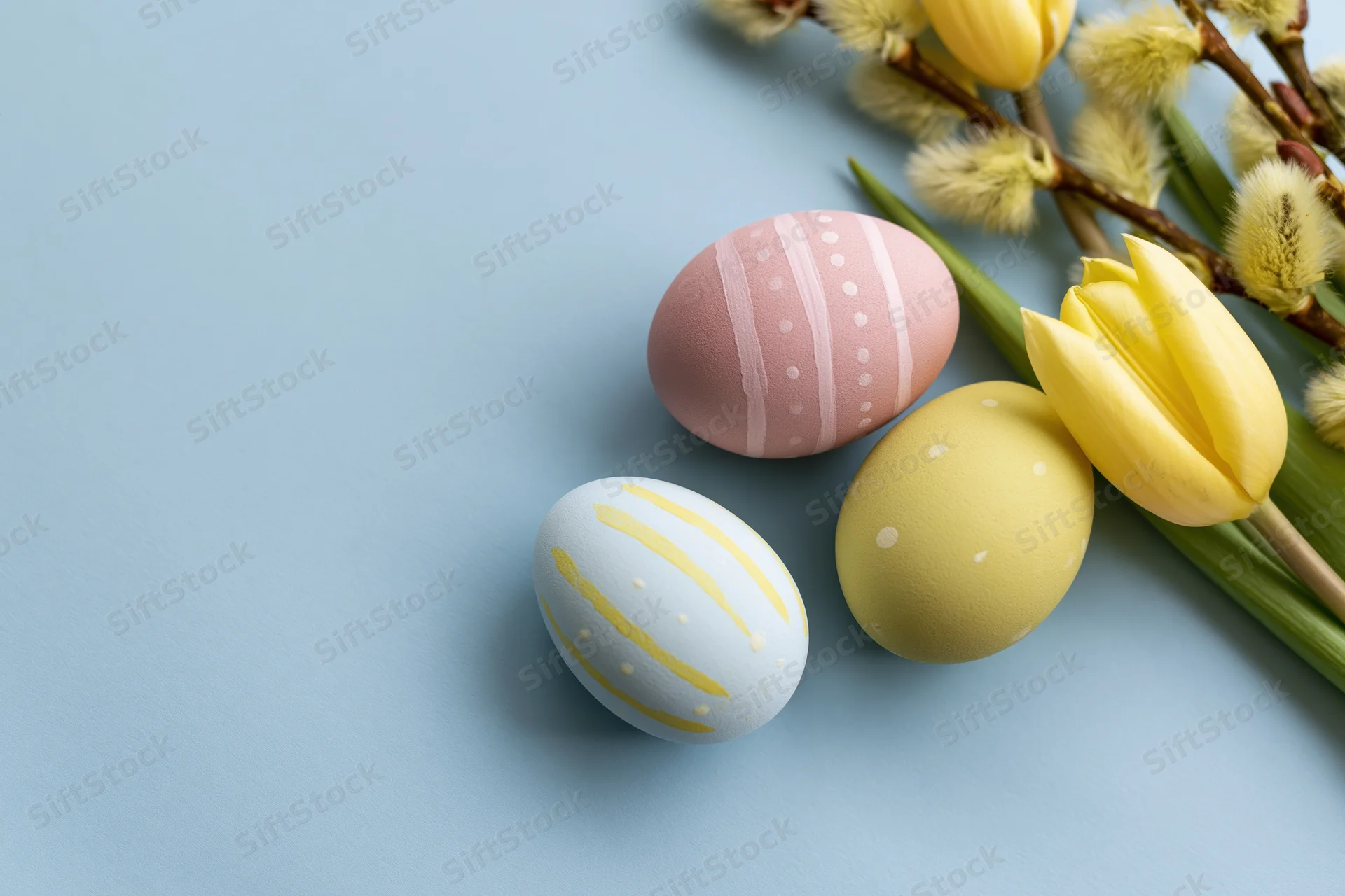 Three hand-painted easter eggs with tulips and willow branches arranged on a blue surface