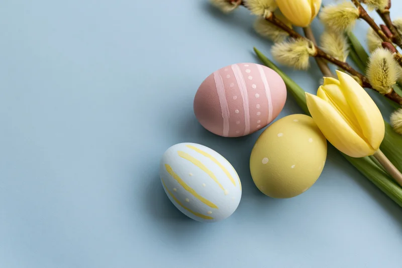Three hand-painted easter eggs with tulips and willow branches arranged on a blue surface