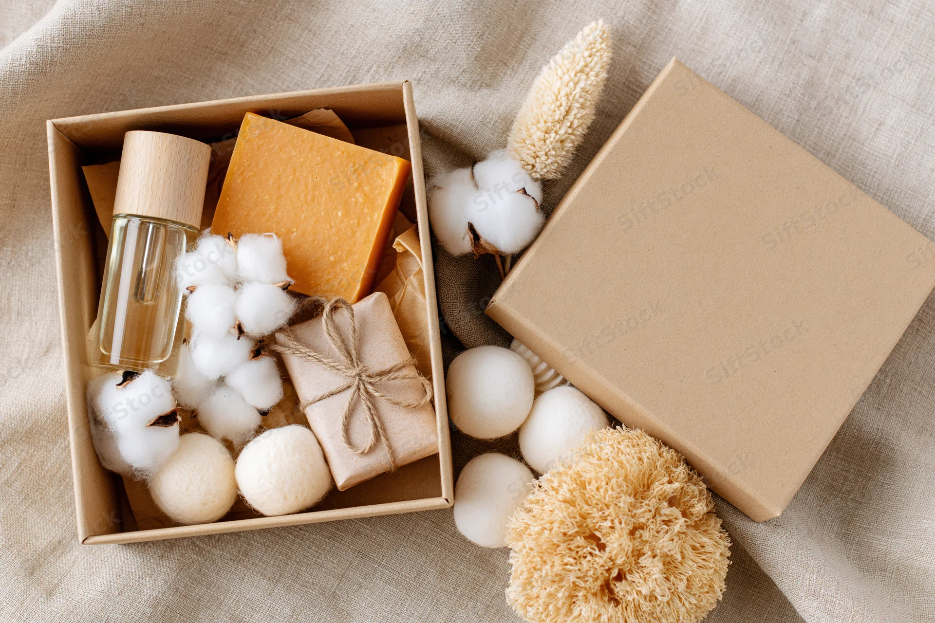 Open kraft gift box filled with natural skincare items and cotton on beige fabric