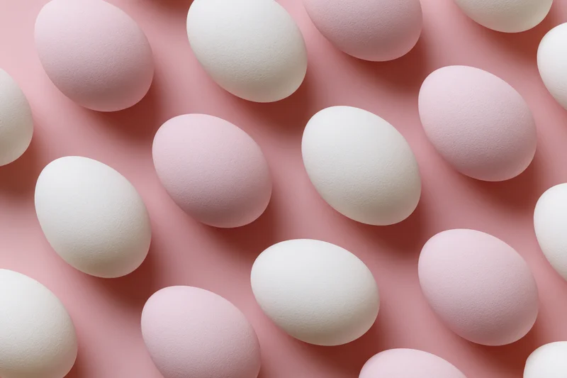 White and pale pink easter eggs arranged in a flat lay overhead composition on a pink surface