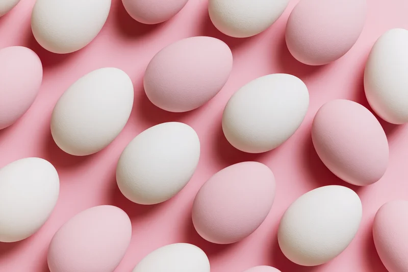 White and pale pink easter eggs arranged in flat lay overhead composition on pink surface