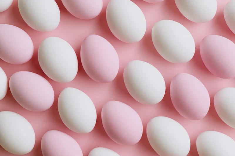 White and pale pink easter eggs arranged in a flat lay overhead pattern on a pink surface
