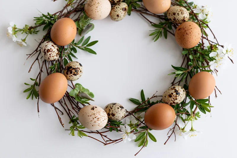 Easter wreath made of twigs greenery and eggs arranged in flat lay on white background