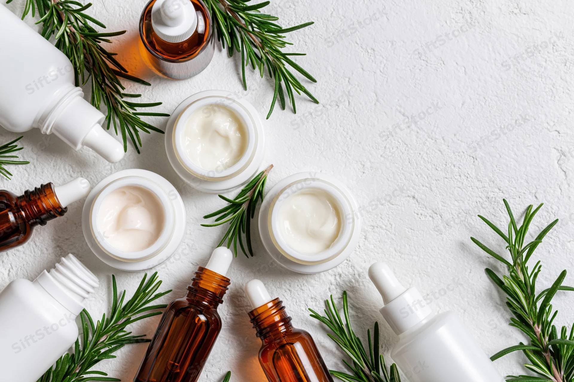 Skincare products arranged in flatlay on white textured surface with rosemary sprigs