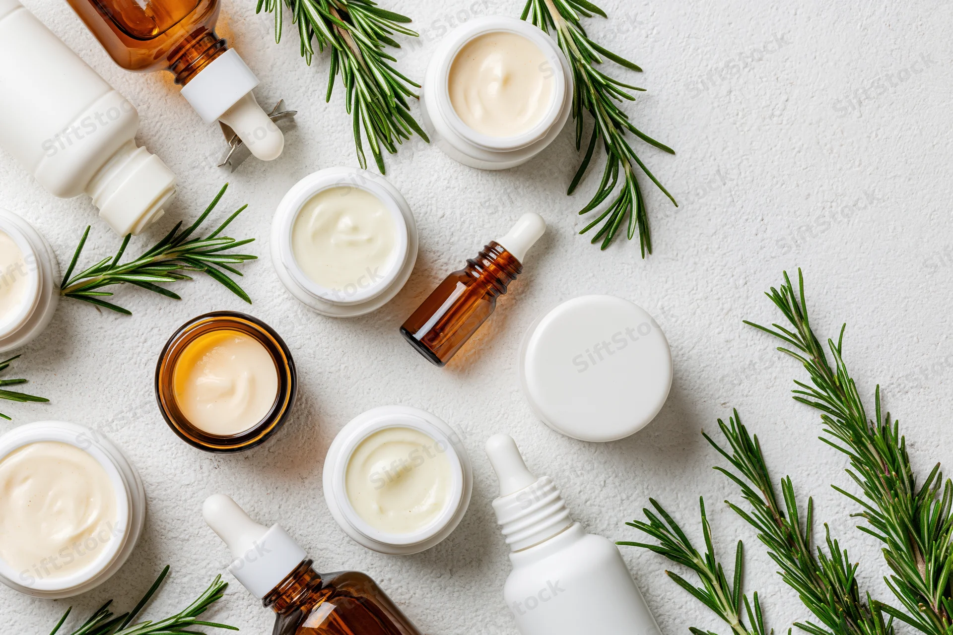 Skincare products arranged in flatlay on white textured surface with rosemary sprigs
