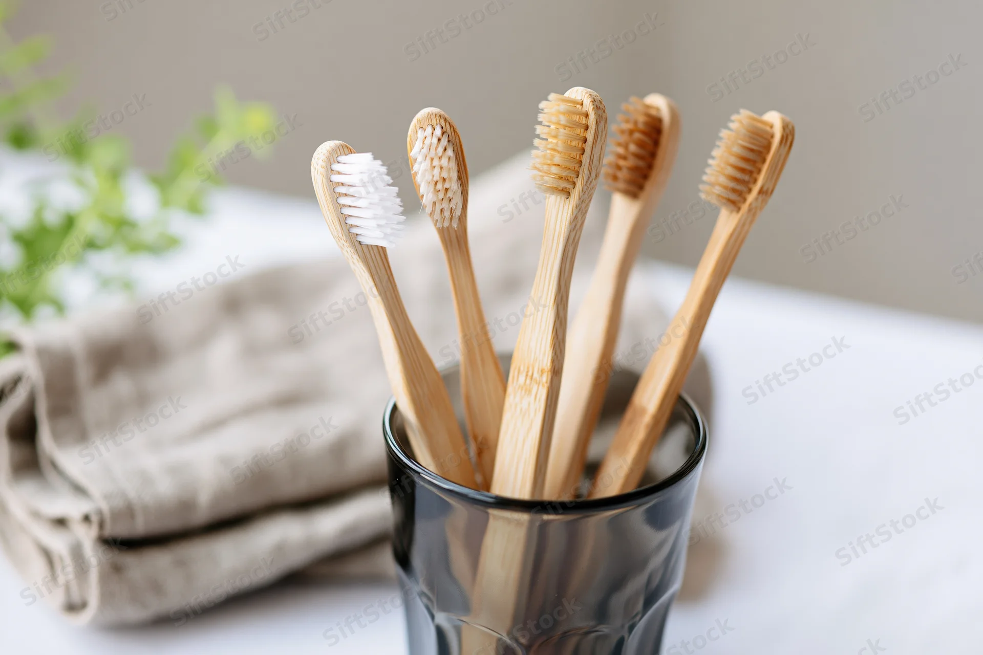 Bamboo toothbrushes with mixed bristle colors standing upright in a black glass cup on a bathroom countertop