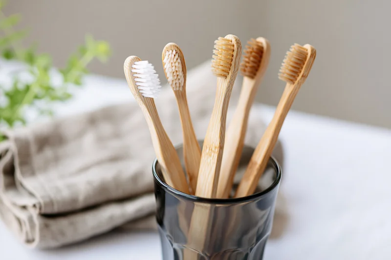 Bamboo toothbrushes with mixed bristle colors standing upright in a black glass cup on a bathroom countertop