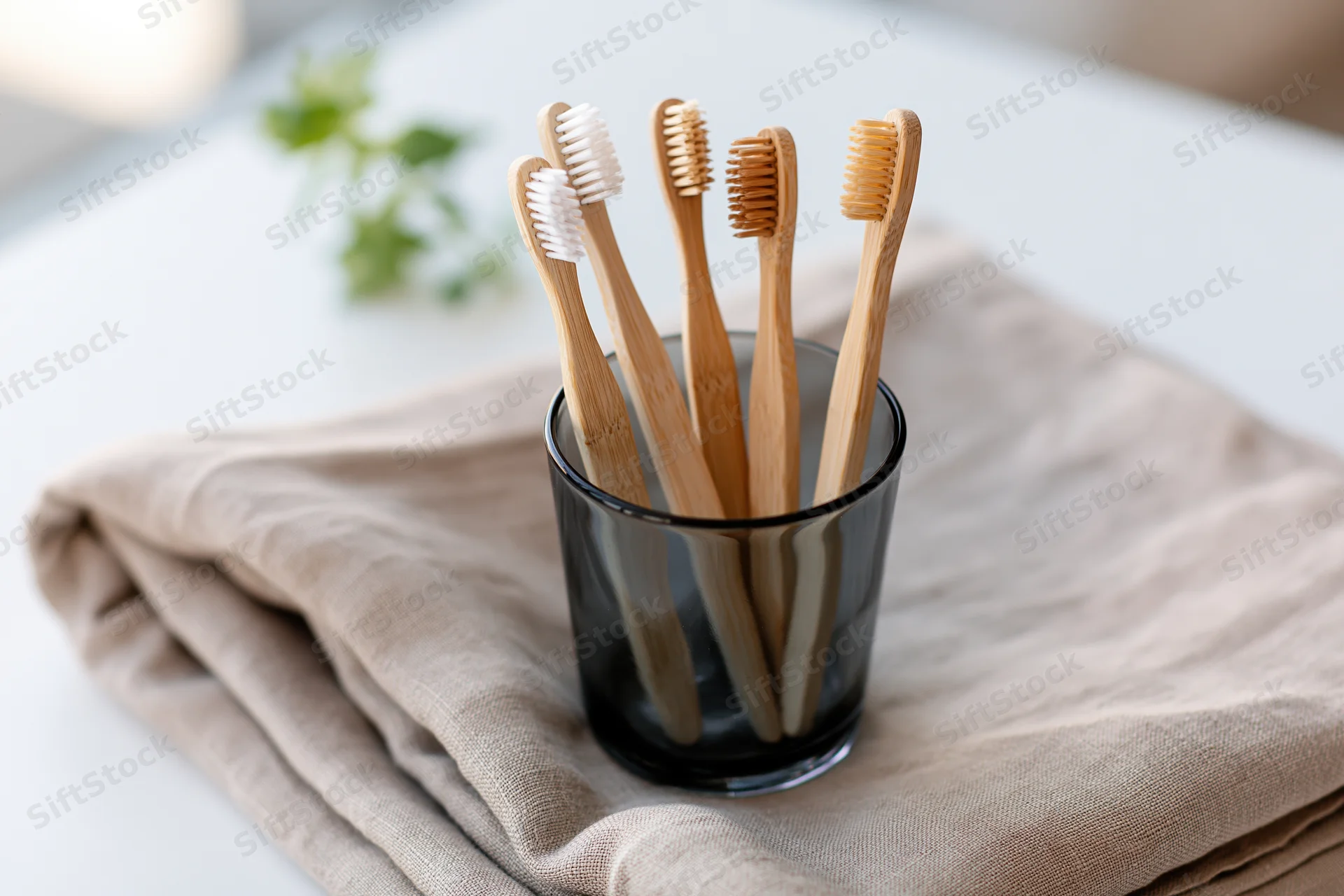 Bamboo toothbrushes with mixed bristle colors standing in a glass cup on a folded linen towel